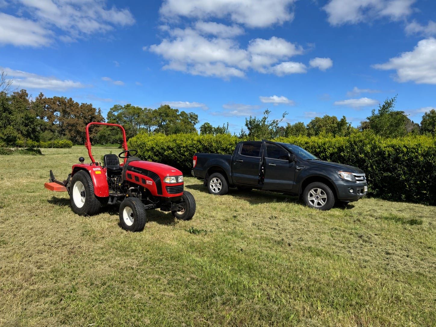 Tractor con implemento de corte y camioneta sobre un campo recién cortado